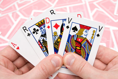 close-up human hands holding four playing cards.