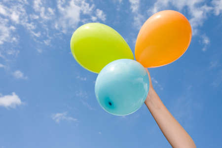 hand with color balloons on sky background.