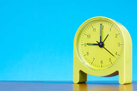 green alarm clock on the table against blue backgroundの写真素材