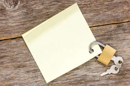 Padlock with empty  sticky note on the wooden background