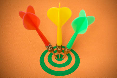 Three darts hitting green target on orange background