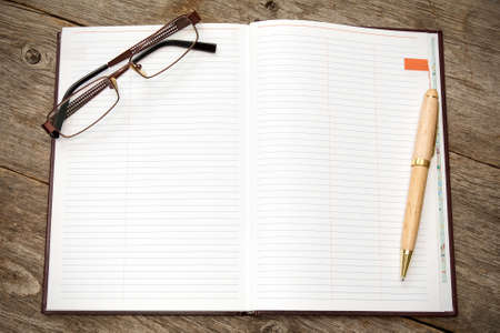 Open notebook with pen and glasses on a wooden background