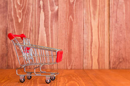 Empty mini shopping cart against brown wooden backgroundの写真素材