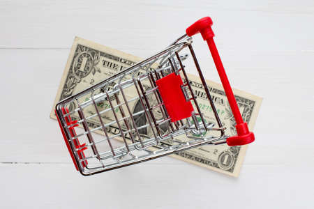 Shopping cart and dollar on the white wooden surfaceの写真素材