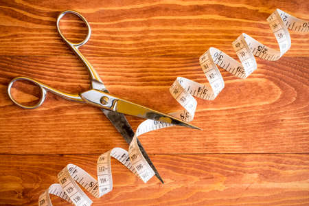 Scissors cutting tape measure on wooden background, concept for slimmingの写真素材