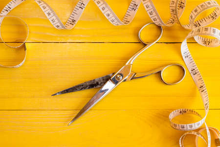 Metal scissors and measure tape on yellow background. Fashion industry concept.の写真素材