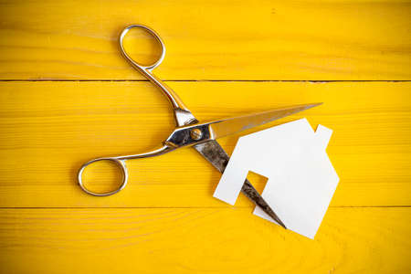 Scissors and house cut out of paper on the yellow background
