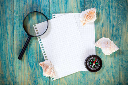 Paper sheets,seashells, compass and magnifying glass on wooden backgroundの写真素材