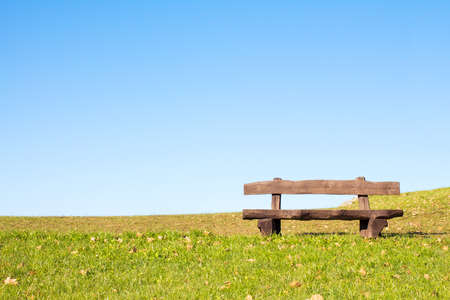 A calm place to rest and relax. An empty wooden bench  over a serene blue sky waiting for a hiker or casual walker to sit and rest.の写真素材