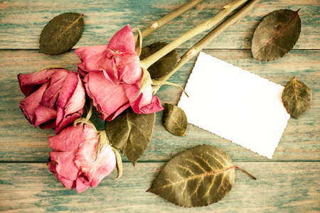 Old roses bouquet and blank greeting card over wooden table. Top view with copy spaceの写真素材