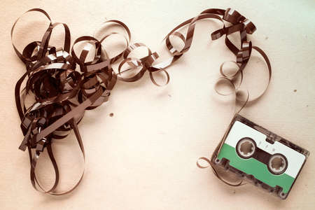 Audio cassette with pulled out tape on stained paper background. Copy-space.