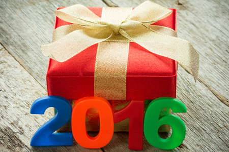 Gift box with golden ribbon and a 2016 sign on wooden background
