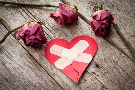 Broken paper heart and old roses on wooden background