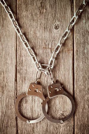 Handcuffs hanging on the chain against old wooden wall.