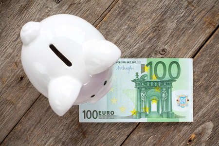 White piggy bank with 100 euro on wooden surface. Top view.の写真素材