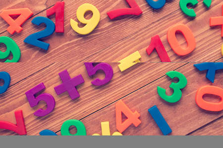 Five add five, simple math addition on wooden background. Cross processed to create retro effect.