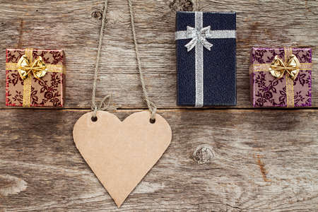 Blank heart shaped tag and three gift boxes on wooden background