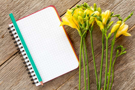Yellow freesia flowers and blank notebook on wooden backgroundの写真素材
