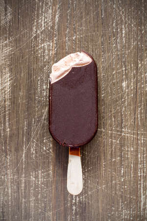 Bitten chocolate covered vanilla ice cream bar on a wooden stickの写真素材
