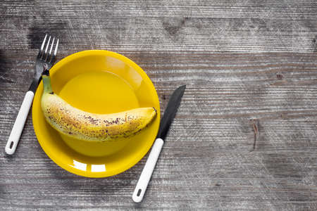 Fork,knife and yellow plate with banana on wooden background.Top view,copy-space.の写真素材