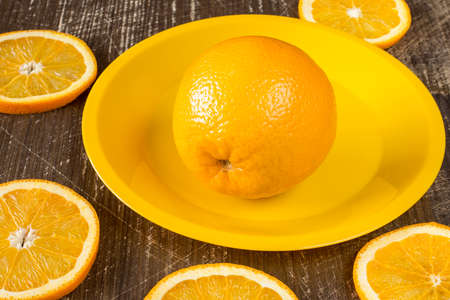 Orange slices and  whole orange fruit on a yellow plateの写真素材