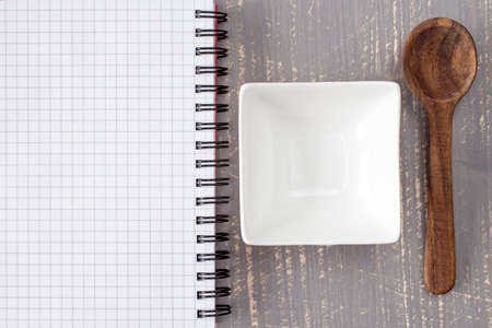 White bowl with spoon and blank notebook on wooden backgroundの写真素材