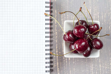 Bowl of fresh cherries and blank notebook for recordingの写真素材