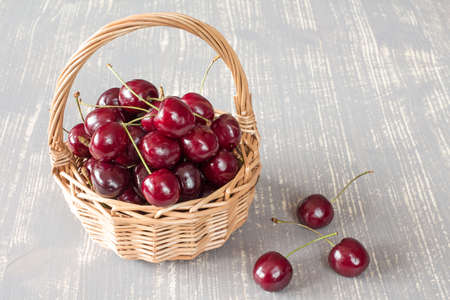 Wicker basket full of fresh cherry fruit on the grey wooden surfaceの写真素材