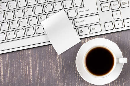 Blank sticky note on  keyboard arranged with cup of coffee