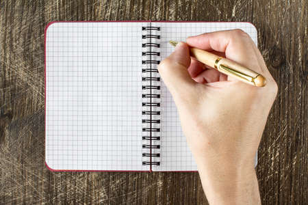 Hand is writing in a notepad on a wooden table