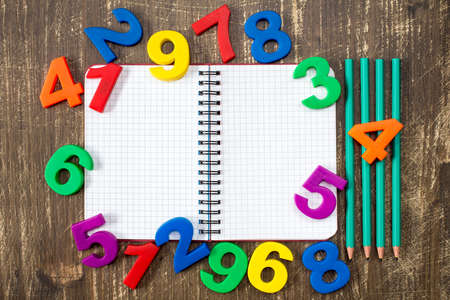 Open notebook with four pencils and colored numbers on the wood background
