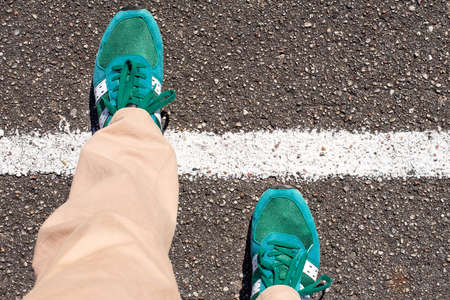 A pair of feet taking a step on an asphalt road across a white line. Concept of achievement.