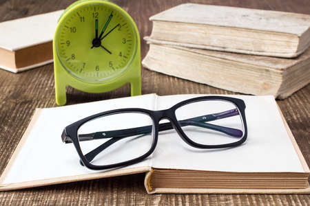 Books with glasses and alarm clock on the deskの写真素材