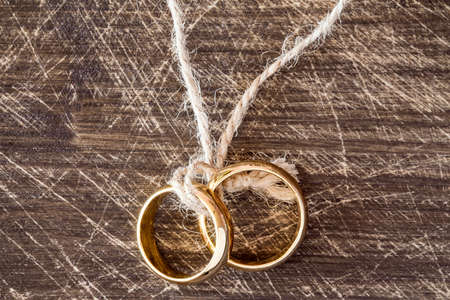 Wedding rings hanging on rope over wooden background.