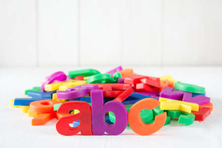 ABC spelling and pile of colorful plastic letters on white wooden backgroundの写真素材