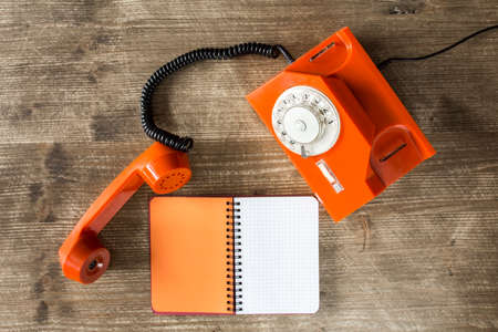 Old orange telephone and blank notebook on wooden table. Top view.の写真素材