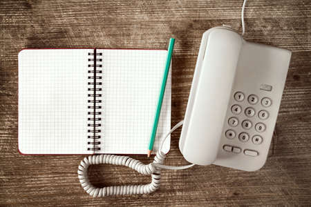 Old grey telephone and blank notebook on wooden table.の写真素材