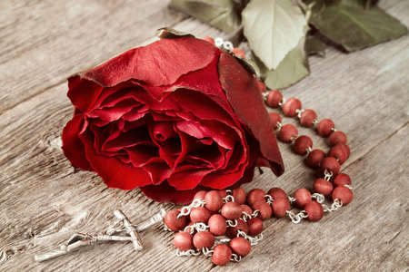 Catholic rosary and red rose on old wooden backgroundの写真素材