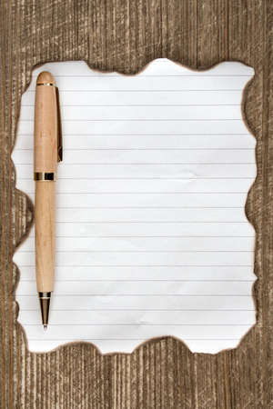 Burned paper sheet with a pen on a wooden table top