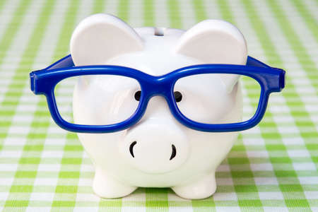 Piggy bank with blue glasses on checkered tablecloth の写真素材
