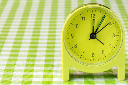 Green alarm clock on the table with checkered tableclothの写真素材