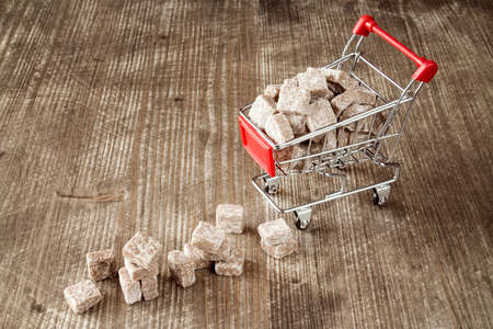 Shopping cart with brown cane sugar  on wooden backgroundの写真素材
