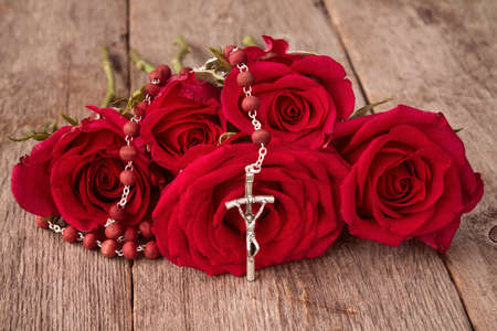 Silver crucifix and bunch of red roses on wooden backgroundの写真素材