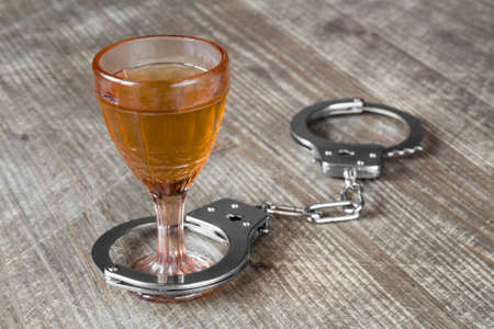 Glass of alcohol with handcuffs as symbol for alcohol abuseの写真素材