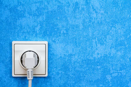 Electrical plug connected into the socket on blue wall
