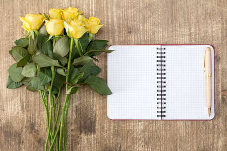 Blank notebook and bunch of yellow roses on the wooden tableの写真素材