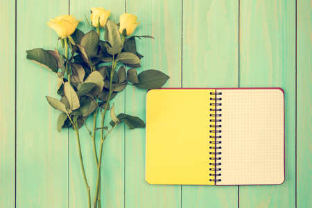 Blank notebook and three roses on the blue wooden backgroundの写真素材