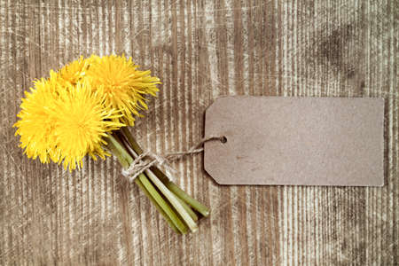 Dandelion flowers with paper tag on wooden table