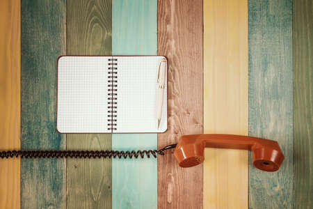 Vintage orange telephone receiver and notebook on wooden background,  top view, pick up the phoneの写真素材