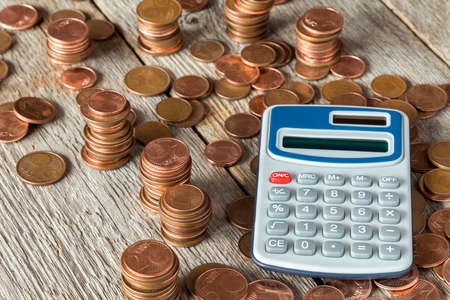 Digital calculator and coins stacked on wooden backgroundの写真素材
